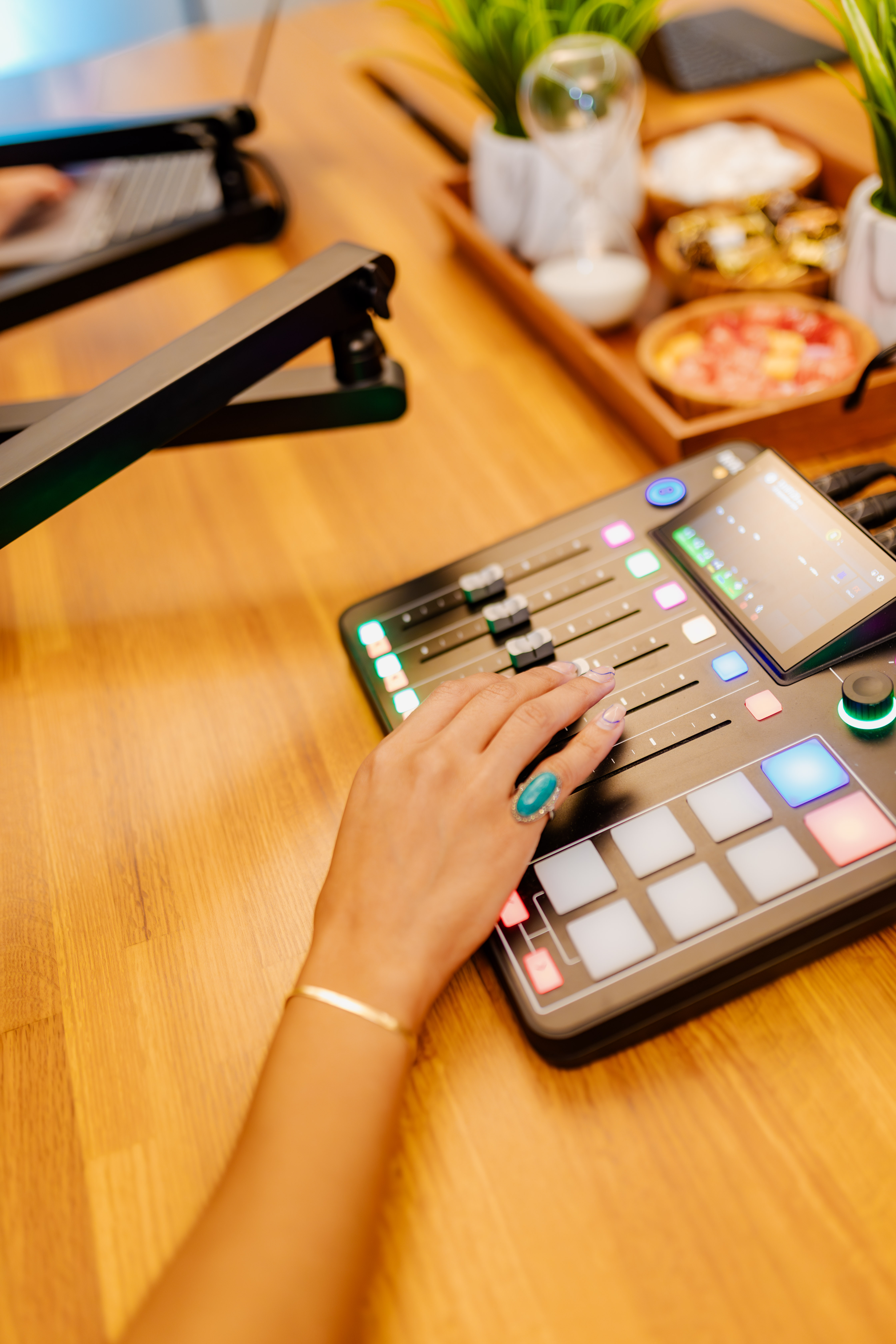 Close-up of a hand adjusting faders and pads on a podcast production console on a wooden studio desk at Peachtree Rose Marketing, with a microphone boom arm in frame.
