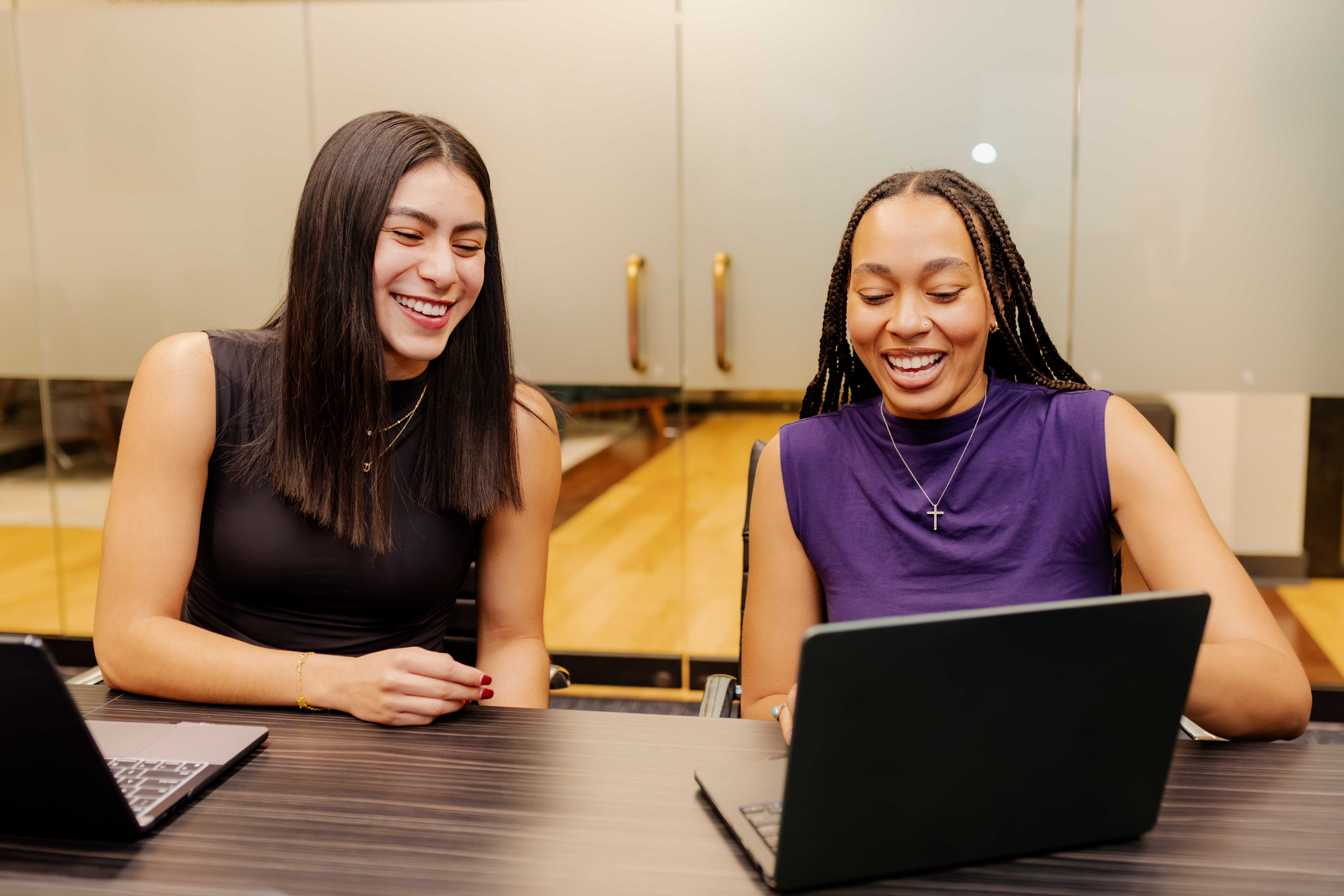 Two Peachtree Rose Marketing team members laughing together while working at laptops, showing genuine connection